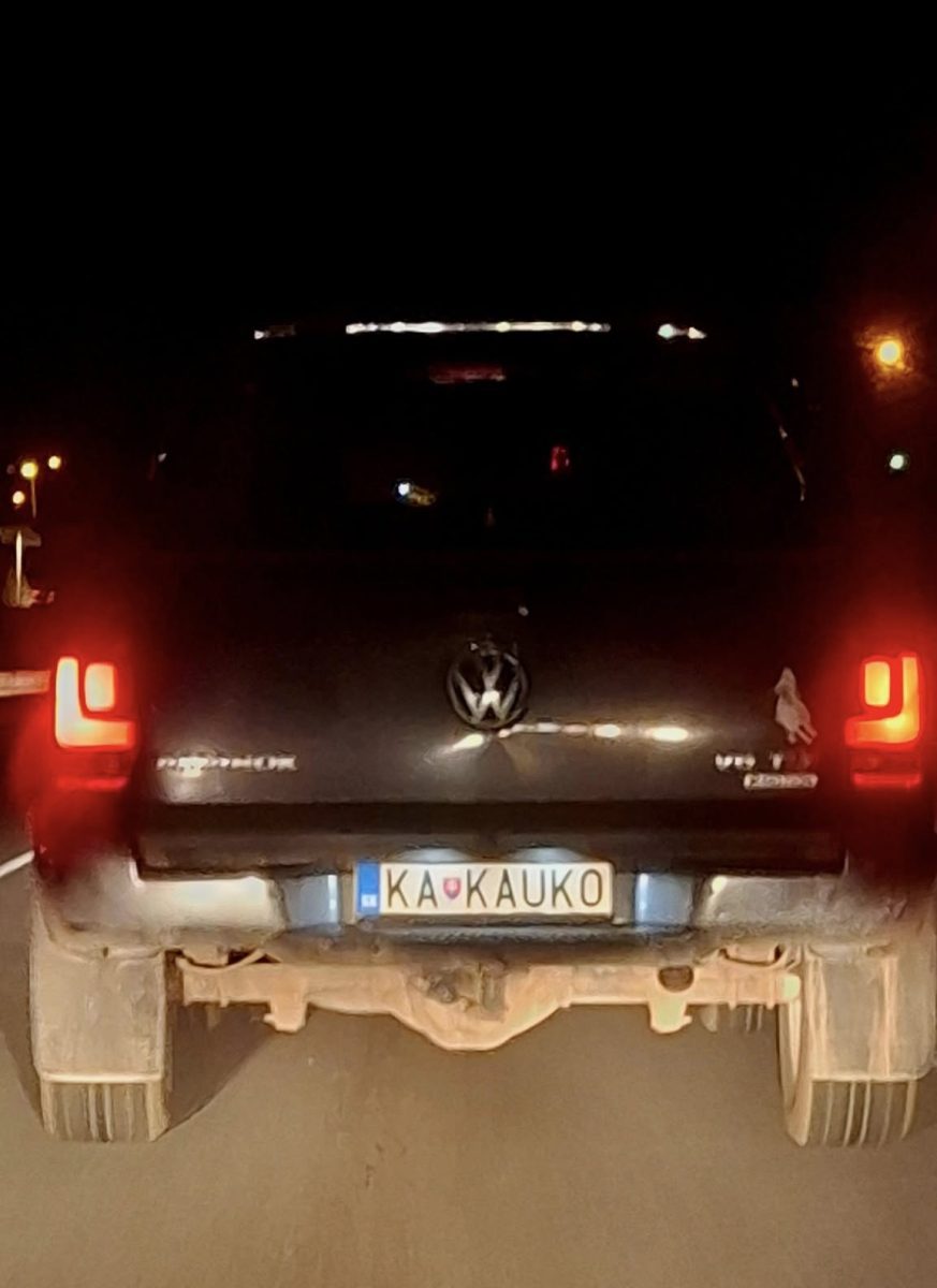 Tmavý Volkswagen s personalizovanou ŠPZ na nočnej ceste, svetlá brzdových svetiel rozžiarené.