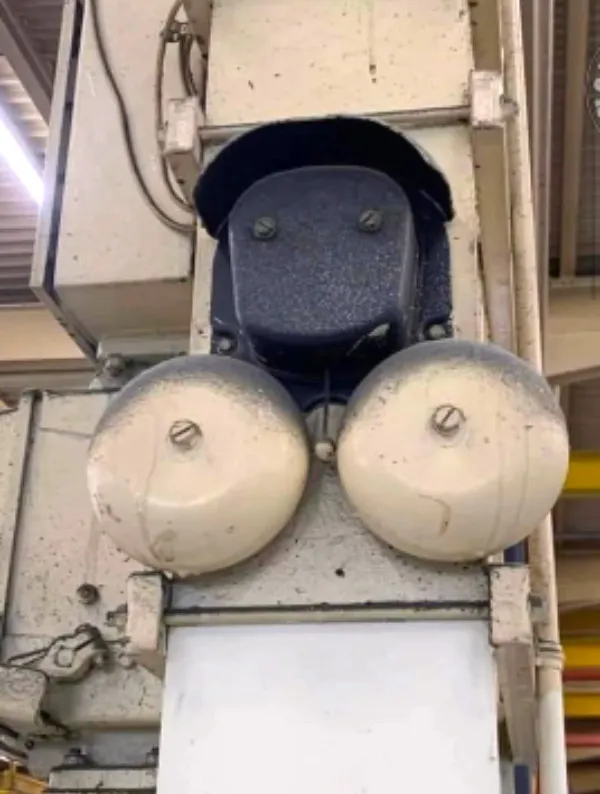 Zariadenie v továrni s dvoma okrúhlymi komponentmi pripomínajúce tvár robota, nad nimi káble.