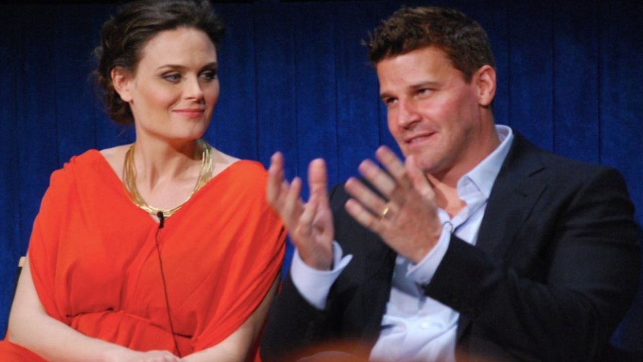 Dvaja ľudia diskutujú na pódiu, žena v oranžových šatách počúva muža v obleku gestikulujúceho s rukami.