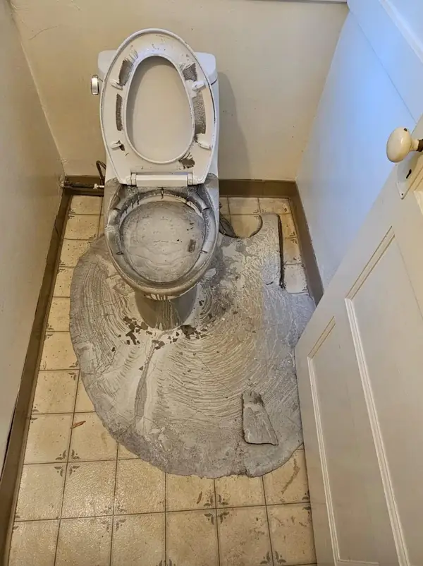 Znečistená toaleta s rozliatym stavebným materiálom na podlahe, pripravená na dôkladné čistenie.