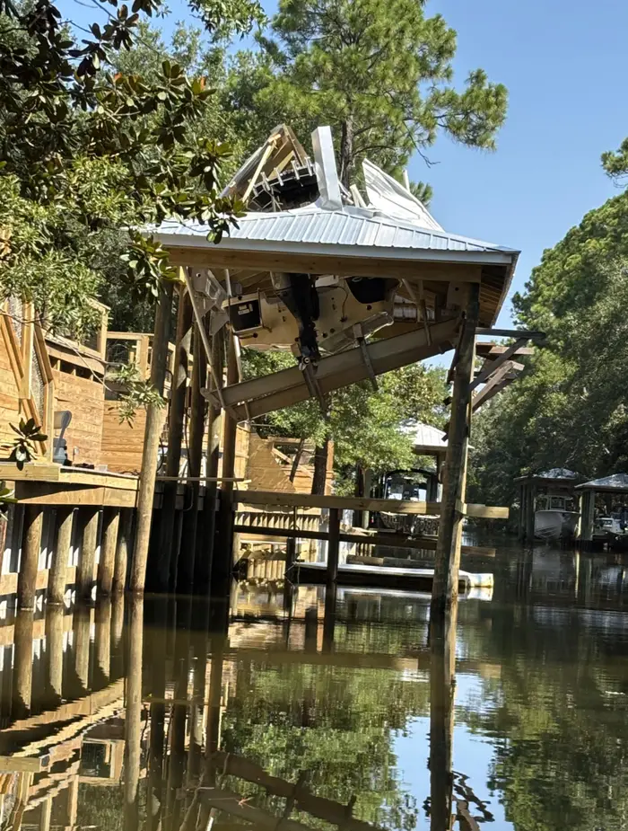 Prevrátený dom nad vodou v prírodnom prostredí, obklopený zeleňou a drevenými konštrukciami.