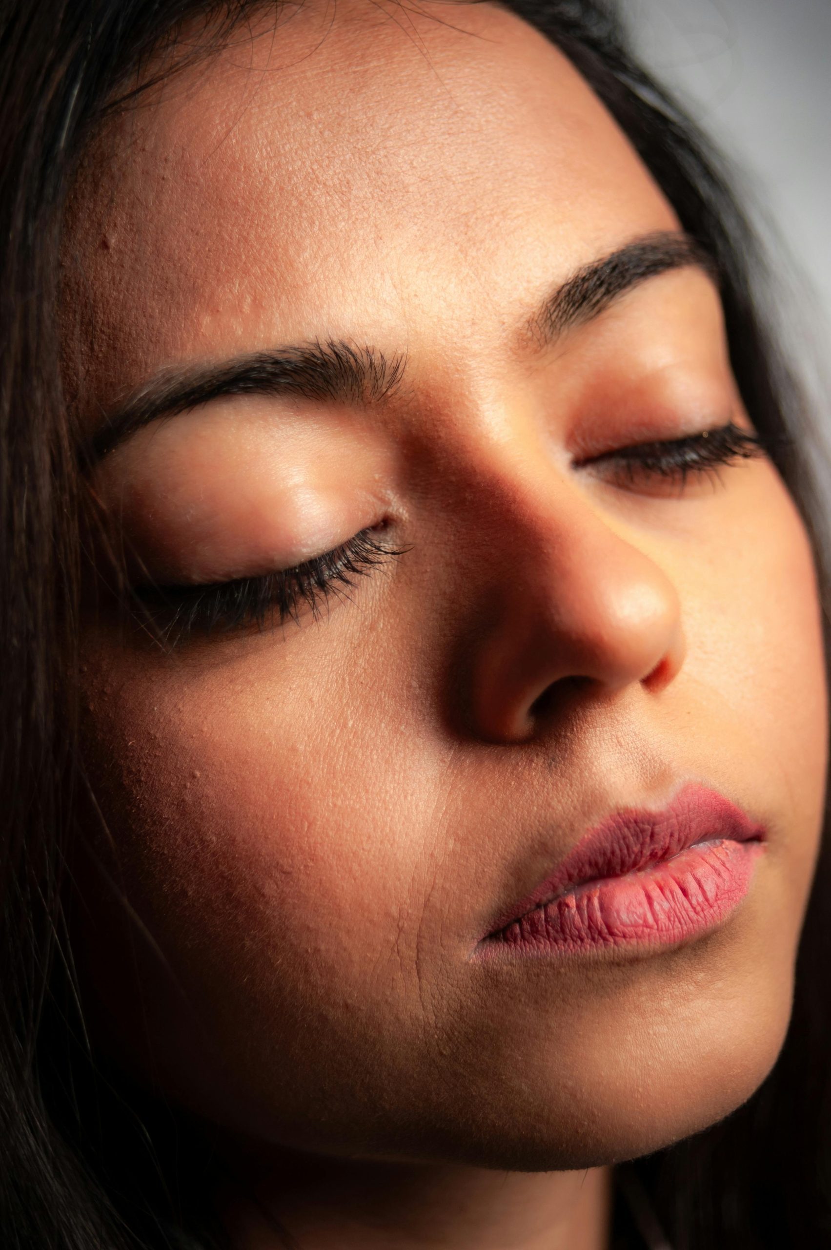 Žena s uzavretými očami v detailnom zábere, zameraná na pokožku tváre a pery.