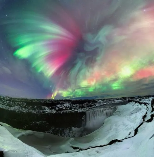Severná polárna žiara nad zasneženou islandskou krajinou, s vodopádom v pozadí za jasnej hviezdnej noci.
