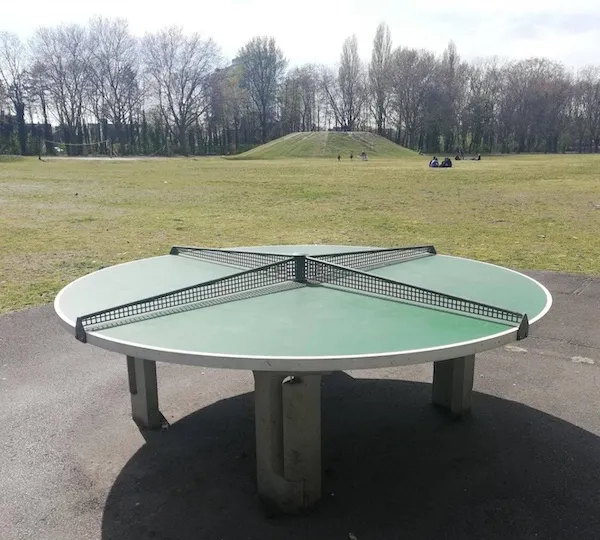 Okrúhly stôl na pingpong v parku s neobvyklým dizajnom, ideálny pre viac hráčov.