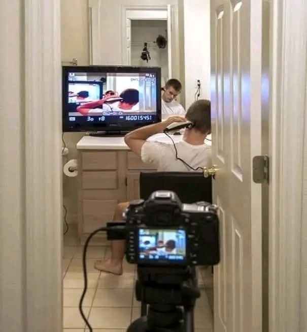 Osoba sa strihá vo vlastnej kúpeľni pomocou kamery a televízora, zrkadlový efekt a obrazovka zobrazujú detaily.