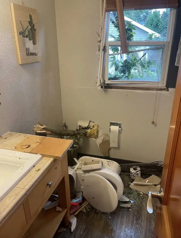 Kúpeľňa s rozbitým oknom a poškodeným záchodom po páde stromu.