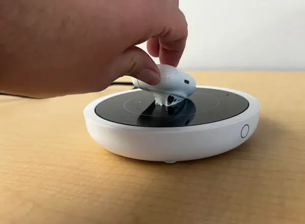 Ruka umiestňujúca bezdrôtový technický doplnok na nabíjaciu podložku na drevenom povrchu.