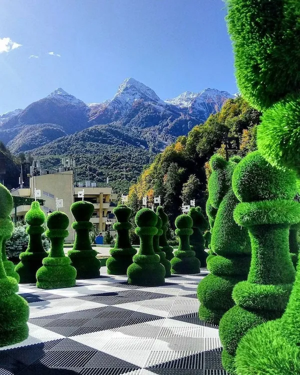 Veľké šachové figúrky v parku s krásným horským pozadím. Pestrá scenéria spája prírodu s hrou.