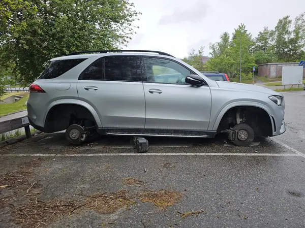 Auto bez kolies zaparkované na parkovisku s zelenou prírodou v pozadí.