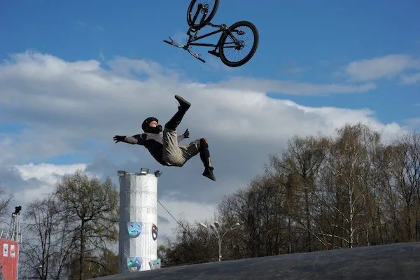 Biker vo vzduchu po skoku z bicykla na rampovom parku pod modrou oblohou, adrenalínový športový výkon.