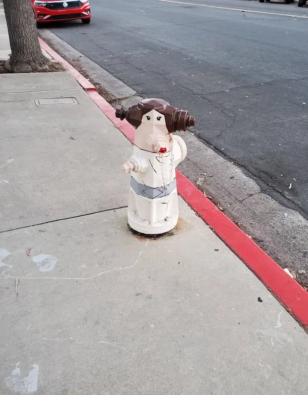 Hasiaci hydrant na chodníku, upravený do podoby fiktívnej postavy s ikonickým účesom z filmového sveta.