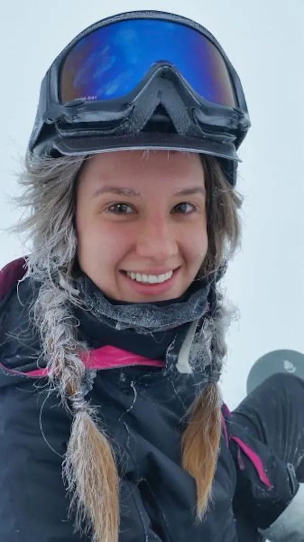 Lyžiarka v zimnom oblečení a prilbe s úsmevom v zasneženej krajine.