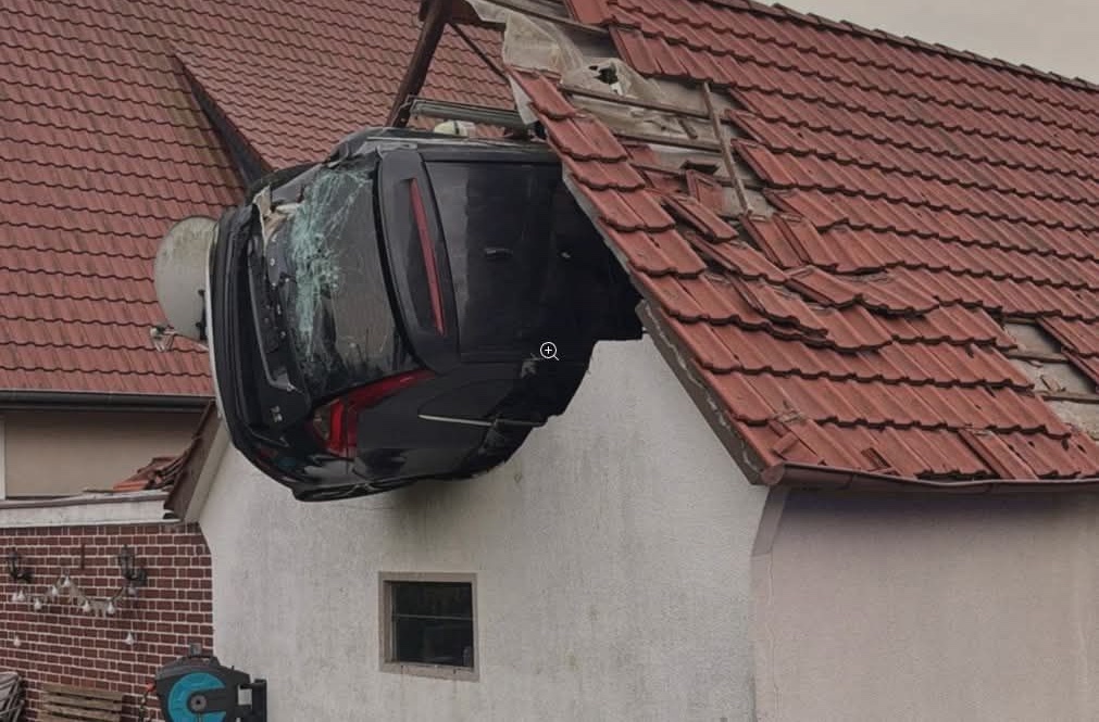 Auto havarovalo do strechy domu, kolesá vyčnievajúce von, značné poškodenie strechy a vozidla.