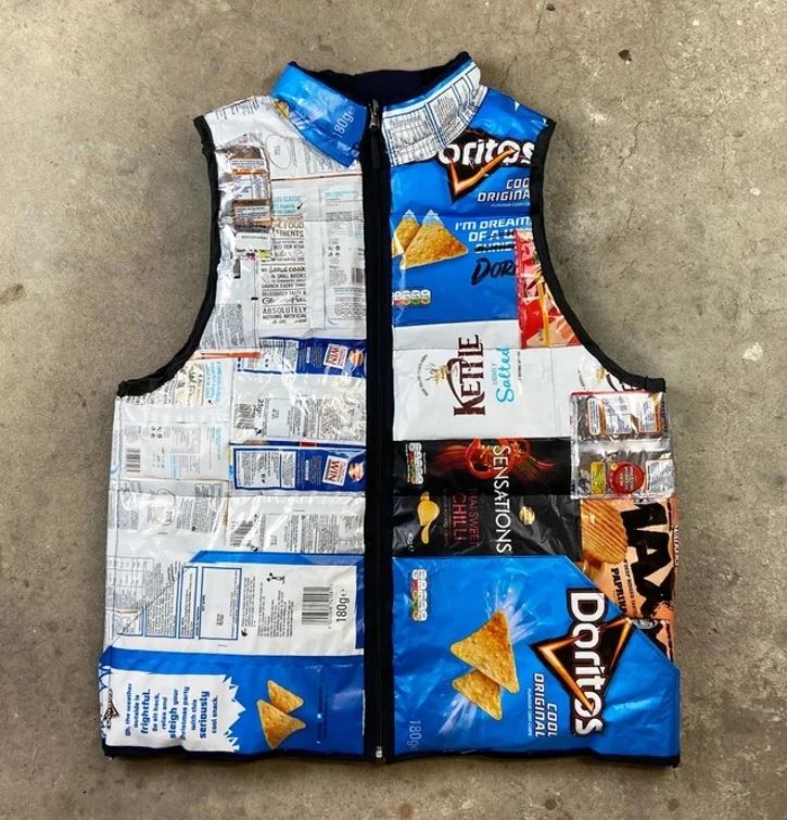 Vesta z recyklovaných obalov od chipsov položená na betónovej podlahe.