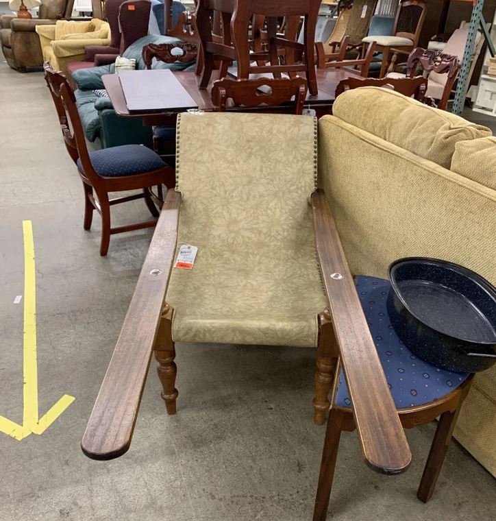 Staré kreslo s drevenými opierkami, obklopené nábytkom v second hand predajni.