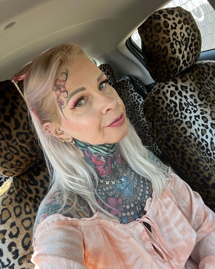 Žena s tetovaniami v aute s leopardím poťahom sedadiel, jemný make-up, ružová blúzka.