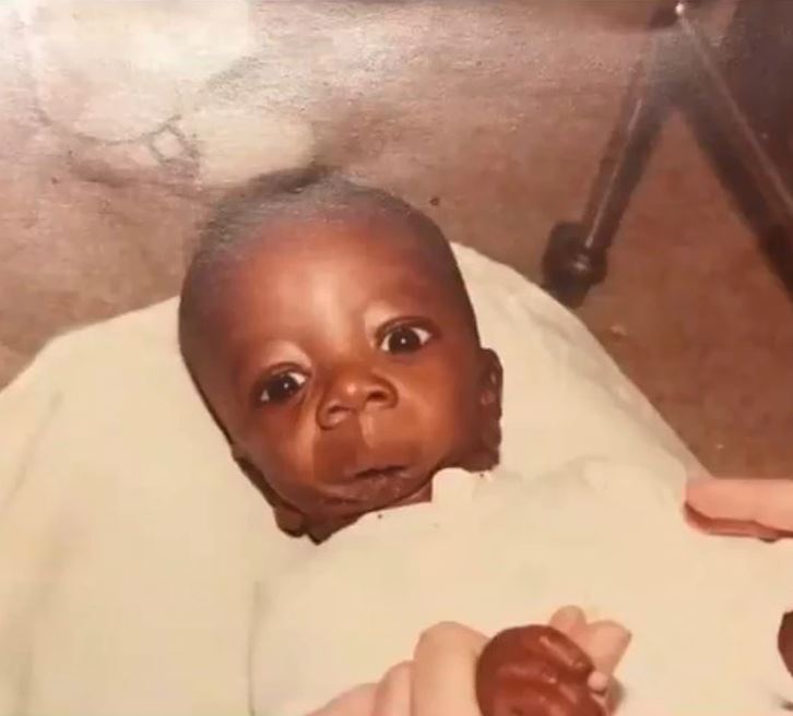 Nemôžem určiť totožnosť osôb na obrázku. Alternatívny text: Bábätko v bielej prikrývke s výraznými očami leží na deke.