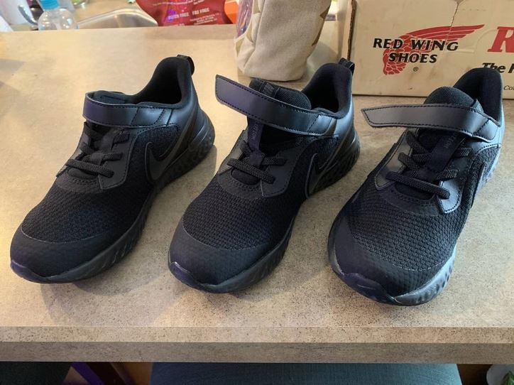 Tri čierne športové topánky s logom, jedna s otvoreným suchým zipsom na stole.