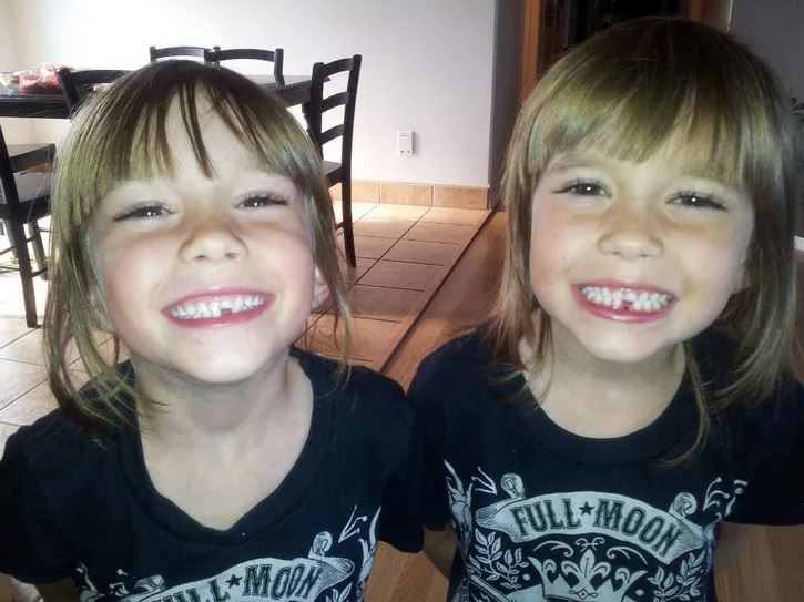 Usmiate dievčatá s podobným účesom v čiernych tričkách stoja vedľa seba v izbe.