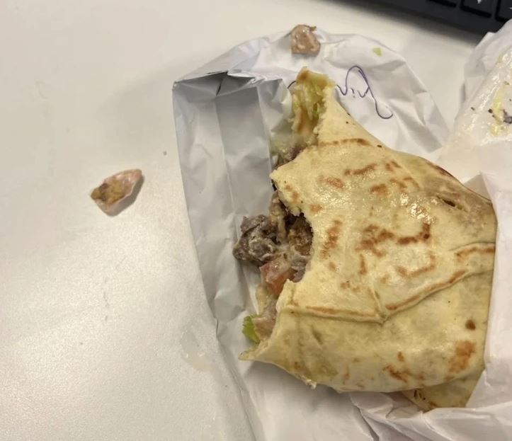 Obedový wrap na stole, čiastočne zjedený, s rozliatou omáčkou a kúskami zeleniny vedľa.