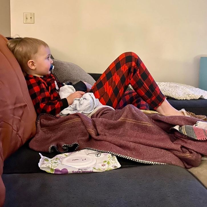 Dieťa v károvaných pyžamách sedí na pohovke, drží sa za deku a pozerá televíziu.