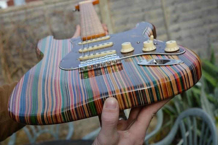 Pestrofarebná elektrická gitara s pruhovaným dizajnom v rukách človeka, pripravená na hranie vonku na dvore.