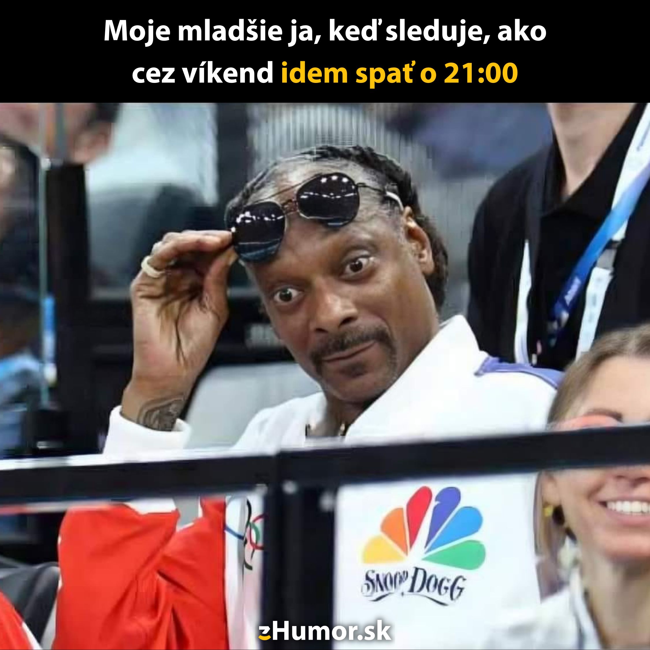 Muž v bielej mikine s logom, zvedavo sa pozerá s nadzvihnutými okuliarmi.