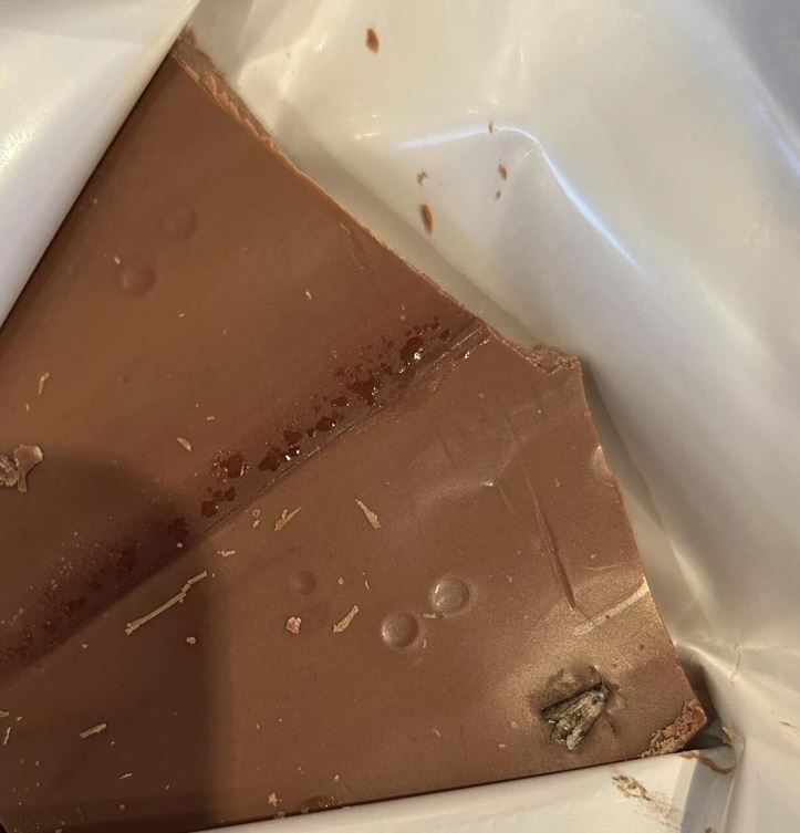 Čokoládová tabuľka s chybou, odkrytý obal a nevhodne umiestnený objekt v spodnom rohu.