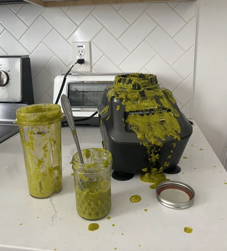 Mixér s rozliatym zeleným smoothie na kuchynskej linke. Neporiadok po príprave nápoja.