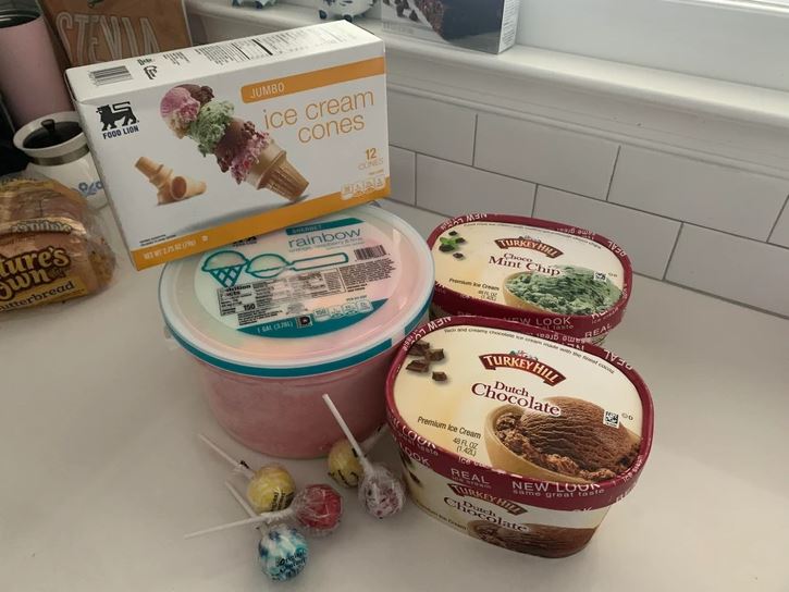 Zmrzlinové kornútky, rôzne príchute zmrzliny a lízatká na bielom kuchynskom pulte pri okne.