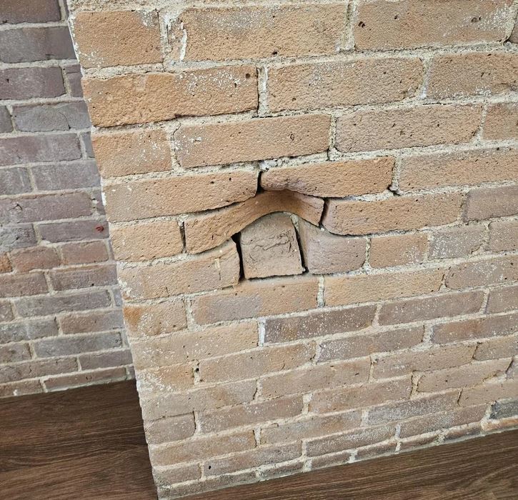 Narušená stena s tehličkami tvaru písmena „U“ v historickej budove, detail drevenej podlahy.