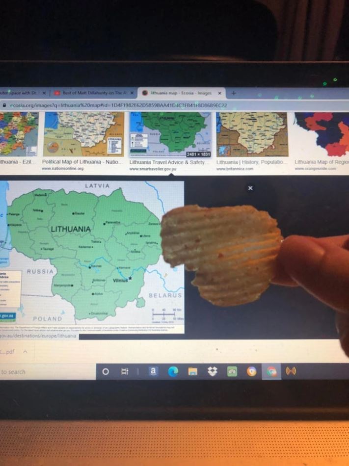 Osoba drží zemiakový lupienok pred mapou Litvy na obrazovke počítača.