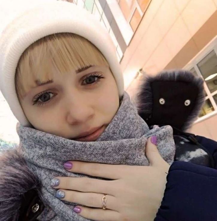 Osoba v zimnom oblečení s farebnými nechtami stojí vonku pred modernou budovou.