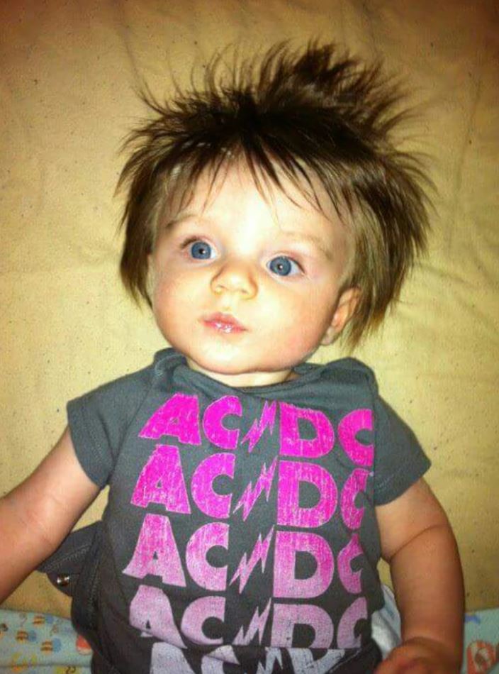 Dieťa s rozcuchanými vlasmi v tričku AC/DC, leží na vankúši.