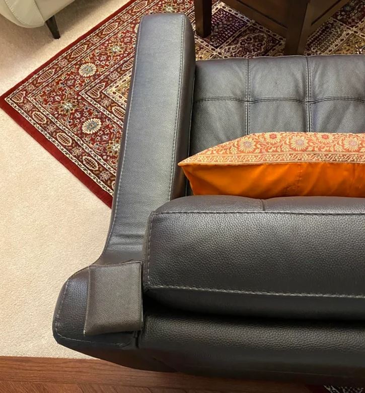 Čierna kožená pohovka s oranžovým vankúšom na dekoratívnom koberci.