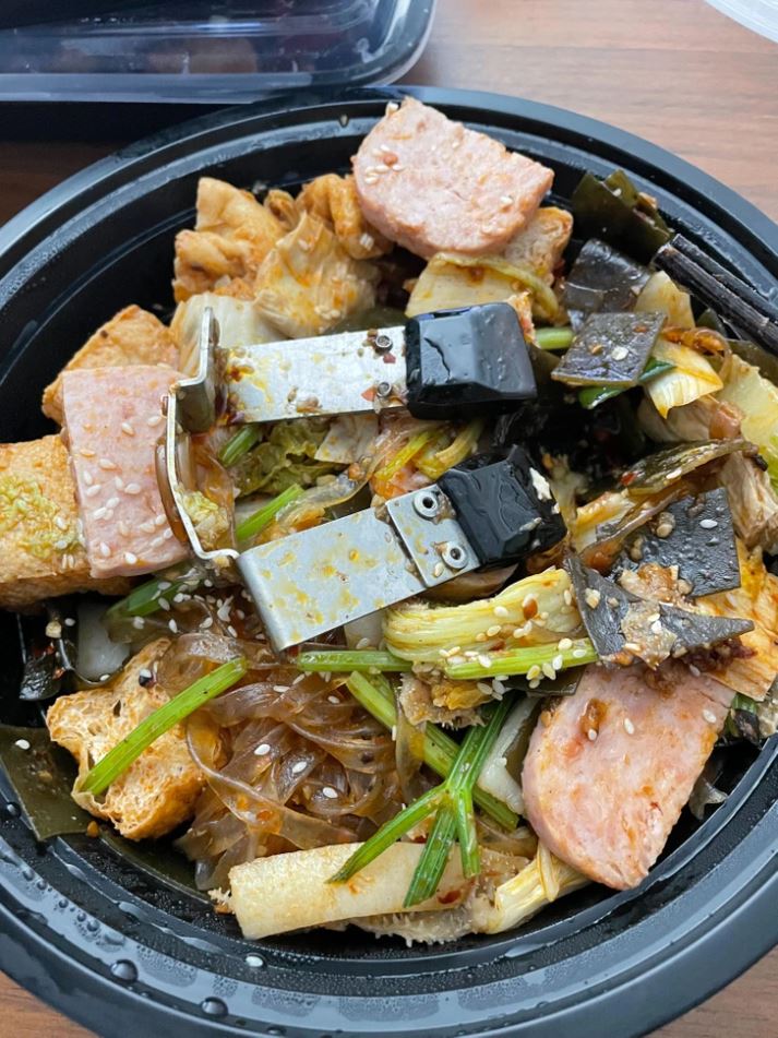 Zmiešaný ázijský pokrm s rezancami, zeleninou a kliešťami na jedlo v čiernej miske.