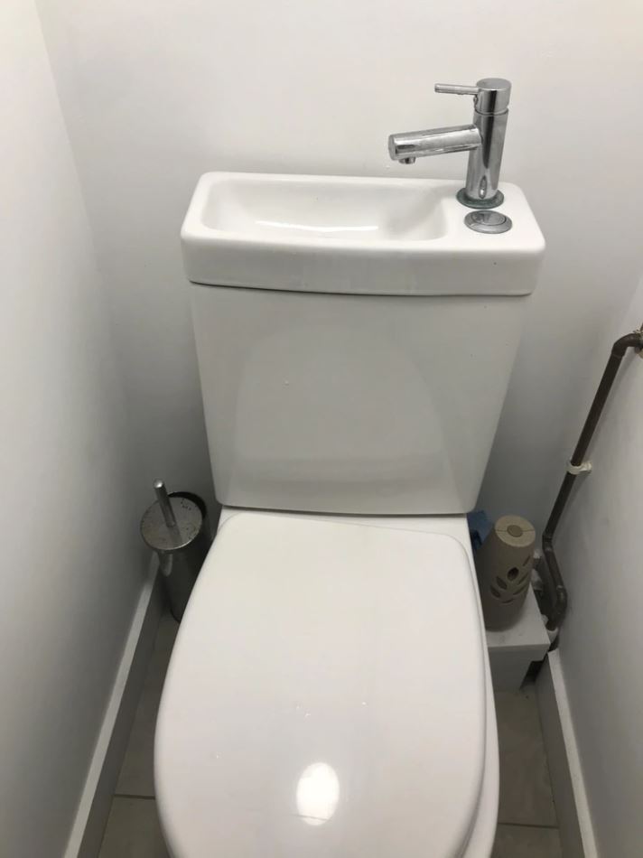 Kompaktná toaleta so vstavaným miniatúrnym umývadlom a kovovým kohútikom v modernom dizajne pre úsporu priestoru.