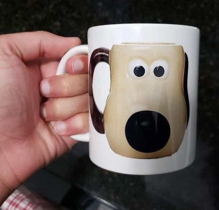 Hrnek s tváří psa v ruke, dizajn inšpirovaný animovaným karikatúrou.