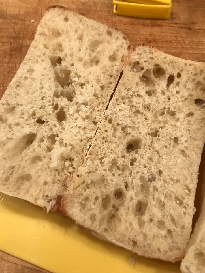 Chlieb na drevenej doske, odkrojený a pripravený na podávanie, s nadýchanou striedkou a zlatistou kôrkou.