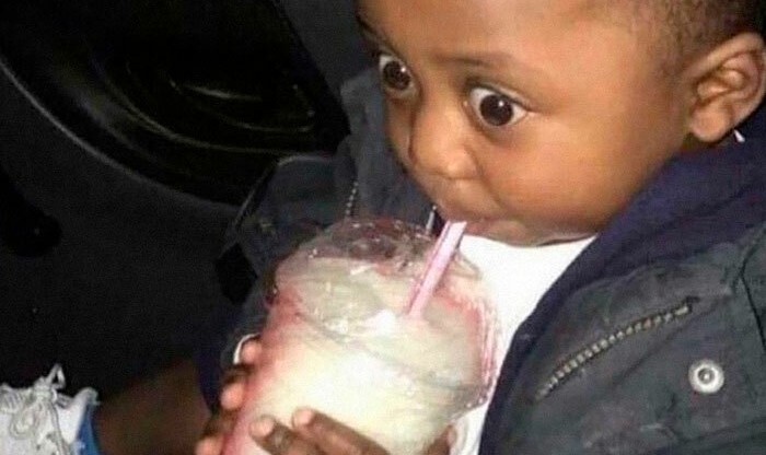 Malé dieťa so široko otvorenými očami pije nápoj zo slamky v aute.