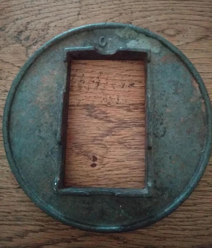 Starodávny japonský tsuba, okrúhly chránicí disk s obdĺžnikovým otvorom, leží na drevenom povrchu.