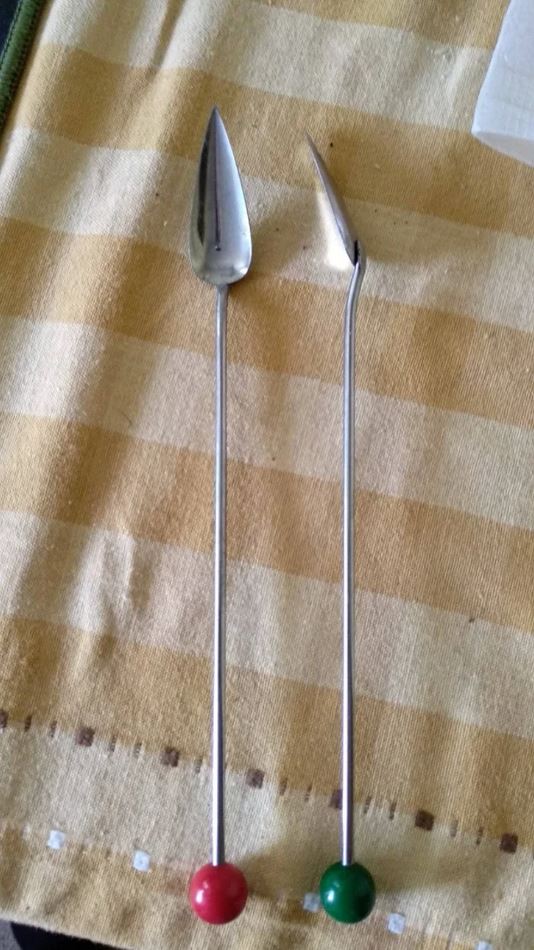 Dve kovové špachtle na prácu s hlinou na žltej deke. Ozdobné guličky na rukovätiach, červená a zelená.