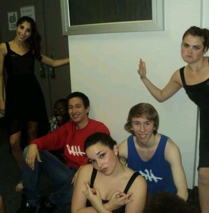 Skupina mladých ľudí pózuje na zábavnom večierku v interiéri, neformálna atmosféra.