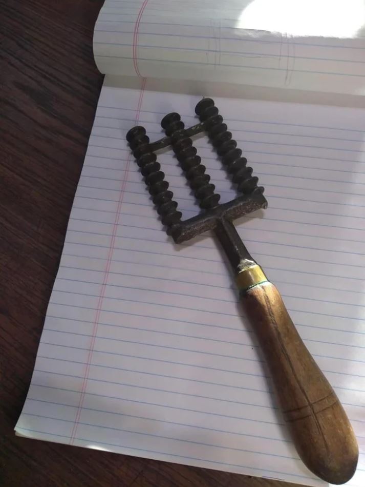 Starodávny kuchynský nástroj s drevenou rukoväťou položený na linajkovanom papieri.