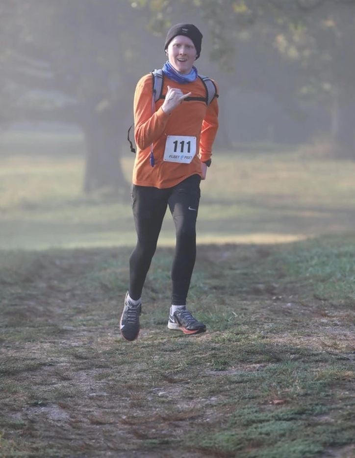 Bežec v oranžovom tričku na vidieckej trase počas hmlistého rána, súťažiaci s číslom 111.