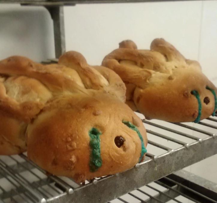 Čerstvo upečené chlebíky s farebnými ozdobami v tvare tvárí na kovovej policovej mriežke v pekárni.