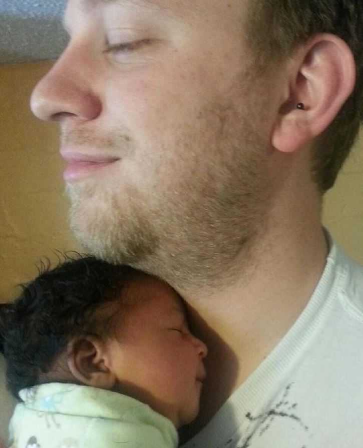 Otec s nežnodržiaci spánkom unavené dieťa na ramene, symbolizujúci otcovskú lásku a bezpečie.