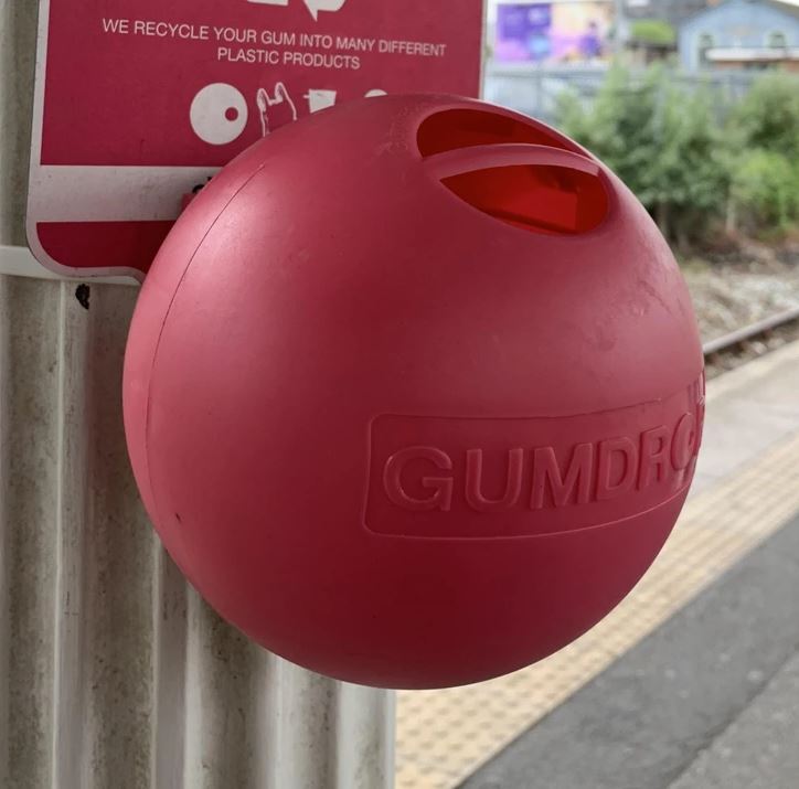 Červená nádoba Gumdrop na recykláciu žuvačiek na železničnej stanici zavesená na stĺpe.