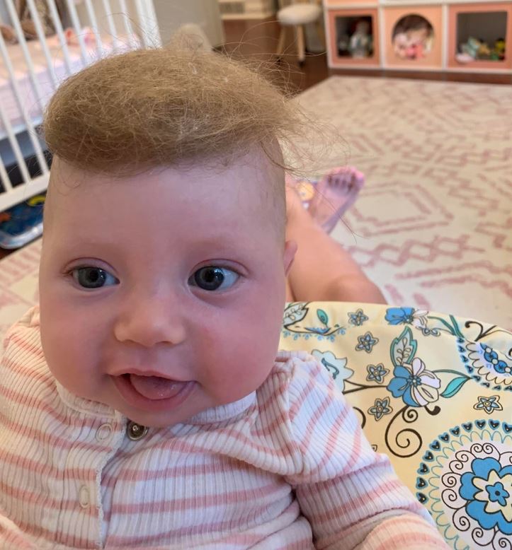 Dieťa s roztomilým účesom a pruhovaným oblečením sedí v izbe s jemným vzorom koberca.