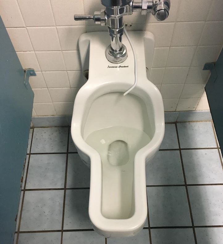 Pisoár s nádržou na vodu v čistom verejnom záchode s dlažbou a kachličkami.